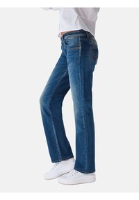 Vaqueros de mezclilla azul con corte recto, ligero desvanecimiento, cinco bolsillos y detalles de costura en color naranja. Combinados con zapatillas blancas.