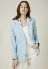 Blazer en coton léger bleu clair avec revers à notch, fermeture à un bouton et deux poches avant, associé à un top blanc et un pantalon blanc.