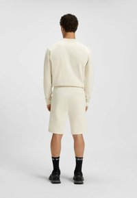 Crème kleurige longsleeve top en bijpassende shorts, met een gladde textuur, casual pasvorm, achteraanzicht, met zichtbare zwarte sokken en schoenen.