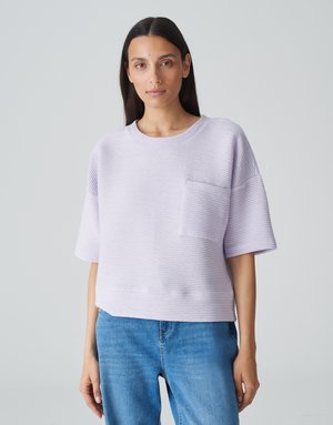 Haut court à manches courtes de couleur violet clair avec une texture côtelée, un col rond et une poche à l'avant. Associé à un jean en denim bleu.