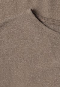 Gros plan d'un tissu beige tricoté montrant la texture et la couture d'encolure d'un vêtement doux et léger.