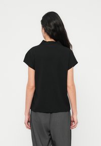 Haut noir à manches courtes en tissu lisse, avec un ourlet légèrement arrondi et une coupe décontractée, associé à un pantalon gris sur mesure.