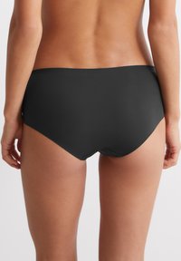 Schwarze Schwimmslips mit einer glatten, matten Textur und niedrigem Bund, die durch klare Linien bestechen und keine sichtbaren Beschläge oder Akzente aufweisen.