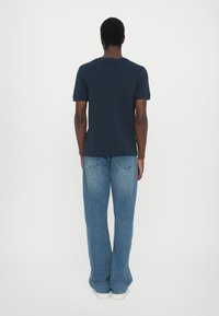 Mørkeblå t-skjorte med korte ermer og rund hals, kombinert med lyseblå vide jeans og hvite joggesko, sett fra ryggen.