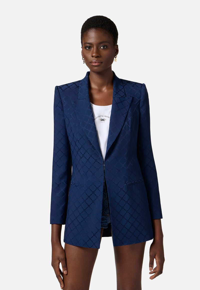 Blazer navy con un motivo a diamante testurizzato, chiusura con un solo bottone, rever affilati e due tasche frontali. Vestibilità sartoriale con maniche lunghe.