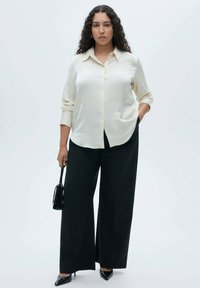 Cremiger Button-Up-Hemd, schwarze weite Hosen, spitze schwarze Absätze und eine kleine schwarze Handtasche. Glattes Material, taillierter Schnitt, minimalistisches Design.