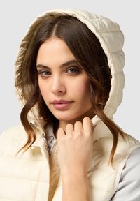 Crème kleurige puffer vest met capuchon, met een geweven ontwerp en een ritssluiting. Zachte textuur en een gladde afwerking zichtbaar rond de kraag.