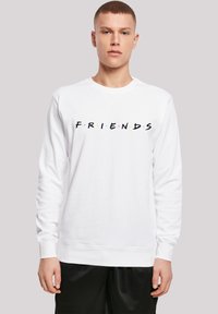 Felpa a maniche lunghe bianca con logo "FRIENDS" in nero e punti colorati. Tessuto morbido, polsini e orlo a coste. Modello che indossa pantaloni corti neri.