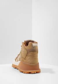 Korkokenkä korkealla varrella, vaaleanruskeaa mokkaa ja verkkoa, jossa on kermaisen värinen pohja, takana vetonauha ja struktuuritetut yksityiskohdat päällä.