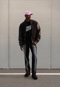 Svart bomberjakke med skinnende ermer, grafisk svart t-skjorte, mørke denimjeans, rosa caps og svarte platformsneakers.