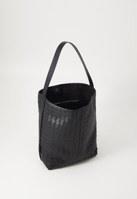 Sac fourre-tout en noir tressé avec une bandoulière en cuir lisse et un corps texturé. Comprend une poche intérieure avec une fermeture éclair.