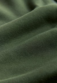 Dunkelgrüner Stoff mit einer glatten, leicht dehnbaren Textur, der ein dezentes, fein gestricktes Muster aufweist, das seine Tiefe verstärkt.