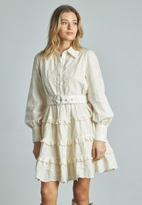 Elfenbeinfarbenes Hemdkleid mit einem strukturierten Blumenmuster, Rüschenschichten, langen Ärmeln und einem runden Gürtel, der die Taille betont.