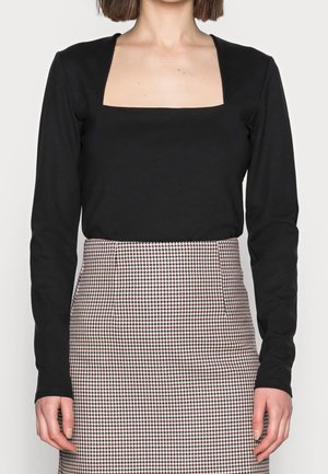 Schwarzes Langarmshirt mit quadratischem Ausschnitt, kombiniert mit einem taillierten Rock im rot-schwarzen Hahnentwistmuster.