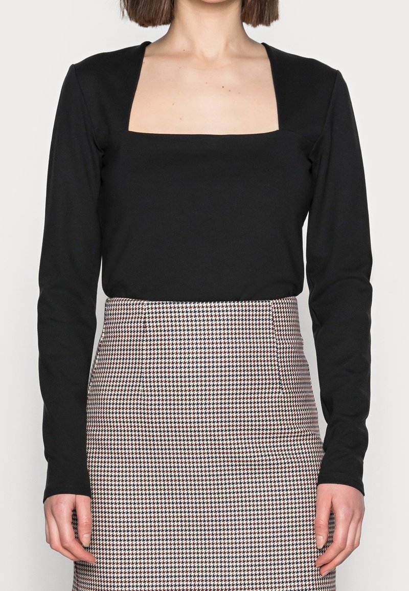 Schwarzes Langarmshirt mit quadratischem Ausschnitt, kombiniert mit einem taillierten Rock im rot-schwarzen Hahnentwistmuster.