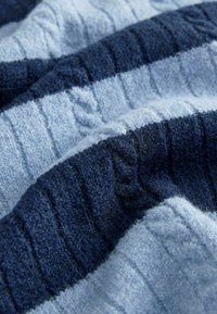 Texturovaná tkanina se střídajícími pruhy v světle modré a tmavě modré. Měkký, huňatý materiál s rýhovaným vzorem a silnou strukturou.