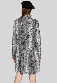 Abito in stampa serpente bianco e nero con maniche lunghe, vita bassa e orlo svasato. Il tessuto ha una texture liscia e una caduta fluida.