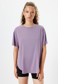 Lilla kortærmet T-shirt med rund hals, løs pasform og glat stof med en let glans, parret med sorte shorts.