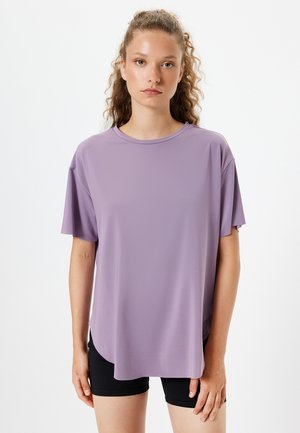 Lila Kurzarm-T-Shirt mit Rundhalsausschnitt, weiter Passform und glattem Stoff mit leichtem Glanz, kombiniert mit schwarzen Shorts.