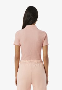 Polo rosa a coste con colletto, maniche corte e design aderente, abbinata a pantaloni jogger rosa coordinati con vita elastica.