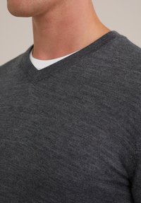 Dunkelgrauer V-Ausschnittpullover mit weicher Textur. Verfügt über einen schmalen Halsausschnitt und ein dezentes Strickmuster, übereinander getragen mit einem weißen Hemd.