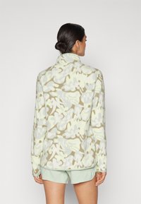 Világoszöld fleece pulóver, bézs és szürke álcázó mintával. Magas gallérral és hosszú ujjakkal rendelkezik, puha tapintású.