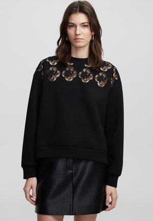 Sweatshirt noir à col rond, doté d'un motif en dentelle le long des épaules et des manches. Le tissu semble doux et texturé.