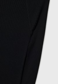 Tessuto a maglia nera a coste, primo piano di una manica con design aderente, che mette in risalto la trama e l'elasticità. Nessun motivo o dettaglio hardware visibile.