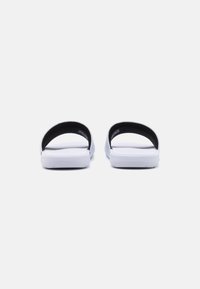 Șlapi albi cu curele negre, având o talpă plată și o branț texturat pentru aderență. Design simplu, minimalist, fără decorații.