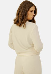 Sweatshirt côtelé couleur crème avec des manches longues, une coupe décontractée et un minimum de couture. Porté avec un bas assorti.