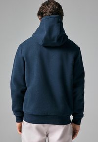Námořnická modrá mikina s kapucí a měkkou texturou, s velkou kapucí, ribbovanými manžetami a elastickým lemem. Bezproblémový zadní design bez grafik nebo vzorů.