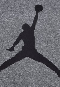 Grått stoff med en fremtredende svart silhuett av en spiller i en hoppende positur, som holder en basketball over hodet.