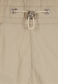 Tissu beige avec une ceinture élastique, des œillets métalliques et un cordon blanc ajustable fixé par un verrou de cordon argenté.