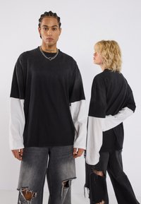 Schwarzes übergroßes T-Shirt mit kontrastierenden weißen langen Ärmeln. Hat einen lockeren Schnitt, weichen Stoff und sichtbare Nähte.