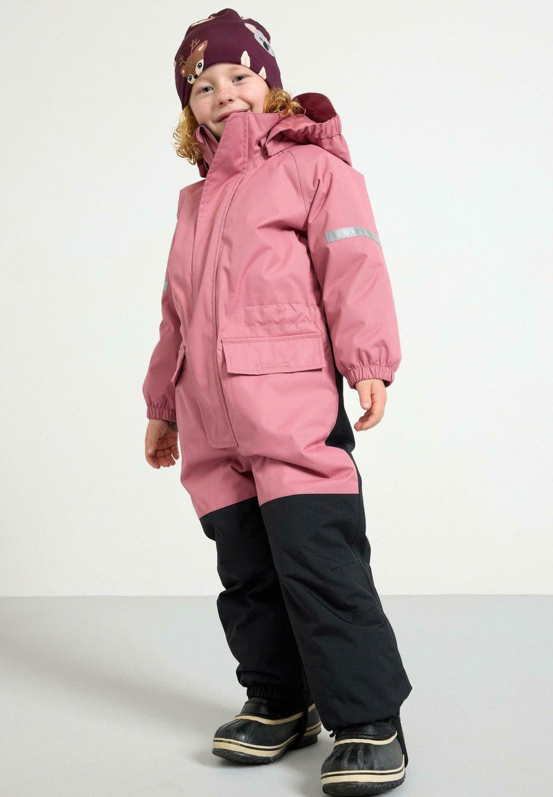 Tuta da neve impermeabile rosa con dettagli grigi, chiusura con zip, due tasche frontali e pantaloni neri sul fondo. Abbinato a un berretto viola con motivo.