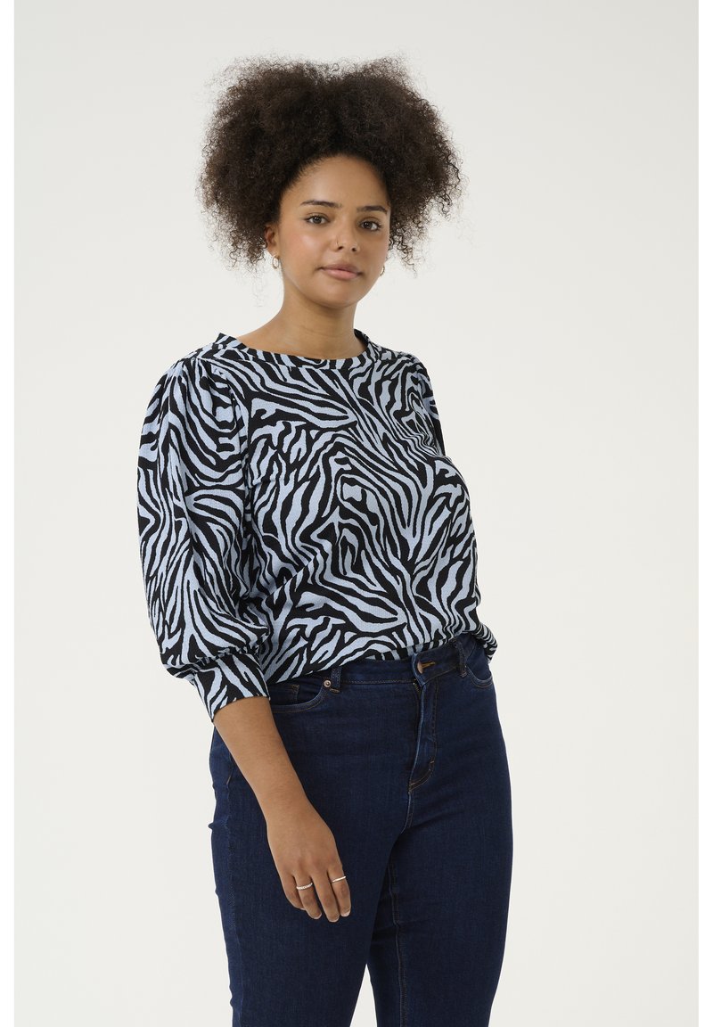 Zebraprint blouse in zwart en lichtblauw met poffende mouwen en een ronde halslijn, gecombineerd met donkere blauwe jeans. Gladde stoftextuur.