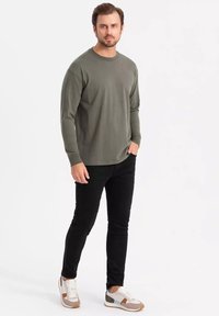 Camicia a maniche lunghe verde oliva, pantaloni slim-fit neri e sneaker multicolori con dettagli grigi, marroni e bianchi. Tessuto dalla consistenza liscia.
