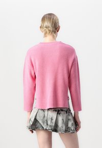Maglione rosa a coste con scollatura a girocollo e maniche a tre quarti, abbinato a una gonna in denim a strisce bianche e nere.