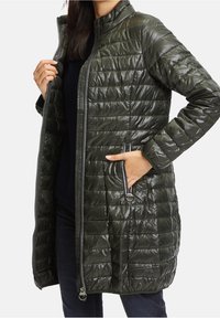 Dlouhý tmavě zelený péřový kabát s lesklou texturou, zapínáním na zip, postranními kapsami a vodorovným prošíváním.