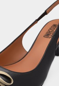 Μαύρο δερμάτινο παπούτσι με λουράκι στο πίσω μέρος, χαμηλό χοντρό τακούνι και μπεζ φιόγκο στη μύτη, ταμπά εσωτερική σόλα με το όνομα της μάρκας.