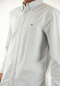 Camicia button-up blu chiaro con strisce verticali bianche. Presenta un colletto, maniche lunghe e un piccolo logo sul petto.