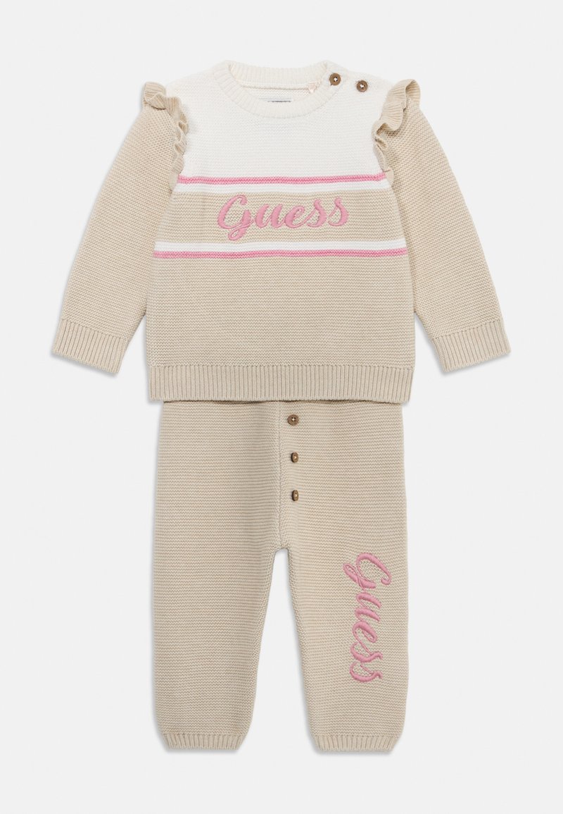 Beige gestricktes zweiteiliges Outfit mit einem Oberteil mit pinkem Logo und Rüschärmeln sowie passenden Hosen mit Knopfdetails und Logoprinz. 