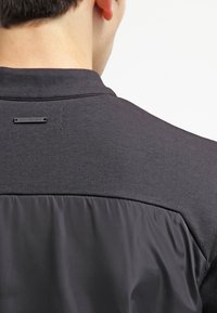 Schwarzes Poloshirt mit einem strukturierten Oberteil und einem glatten, matten unteren Bereich; mit einem kleinen Calvin Klein Logo-Tag.
