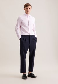 Camicia a maniche lunghe rosa chiaro con collo, abbinata a pantaloni blu navy a vita alta con pieghe e scarpe in pelle nera. Tessuto liscio.
