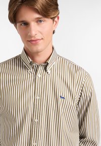 Camicia con bottoni a righe verticali marroni e bianche, con un piccolo logo blu sul petto. Tessuto in cotone con colletto.