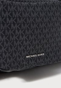 Sötét anyag, ismétlődő szürke "MK" mintával és ezüst "MICHAEL KORS" márkanevével az alján, középen.