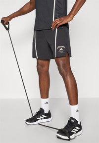 Fekete sportnadrág, fehér oldalcsíkkal, az "Adidas Training Club" logójával. Fekete sportcipővel és fehér zoknikkal viselve.