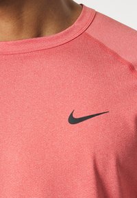 Camiseta deportiva roja hecha de tejido texturizado con cuello redondo. Presenta el logotipo negro de Nike en el pecho y costuras en contraste en las mangas.