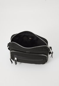 Black fabric crossbody bag with dual zippers, exterior pocket, and smooth texture. Interior is lined with a black material.