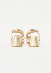 Gullblokk-hælede sandaler med rhinestone-detaljer, åpen bakdel og kryssende stropper. Glatt metallisk finish og teksturerte detaljer.